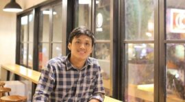 Seorang pria duduk di sebuah kafe modern di Bali, suasana santai ini kontras dengan perhatian publik atas kasus video bermuatan pornografi yang tengah viral dan menjadi sorotan hukum.  