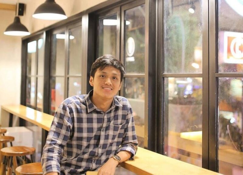 Seorang pria duduk di sebuah kafe modern di Bali, suasana santai ini kontras dengan perhatian publik atas kasus video bermuatan pornografi yang tengah viral dan menjadi sorotan hukum.  